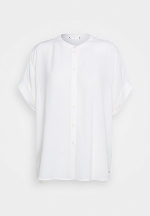 Camisa blanca de botones con escote redondo, mangas cortas y corte holgado. Hecha de tela ligera con una textura suave y un brillo sutil.