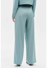 Pantalon large bleu clair avec une texture lisse et une taille haute, présentant des plis subtils et un design propre et ajusté.