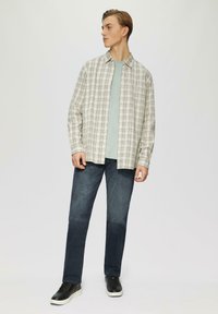 Chemise à manches longues en carreaux blancs et gris sur un t-shirt bleu clair, accompagnée d'un jean foncé et de baskets noires, avec un tissu texturé.