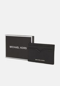 Porte-cartes en cuir noir avec une finition texturée, comportant deux fentes pour cartes et un logo, présenté à côté d'une boîte noire avec une bordure argentée.