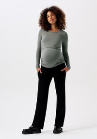 Langemouwen, salie groene zwangerschapstop met ruching in de taille, gecombineerd met zwarte, losvallende broek en zwarte platform schoenen.