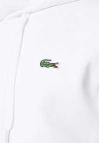 Witte hoodie met een gestructureerde stof. Voorzien van een groen geborduurd krokodillenlogo op de borst. Heeft een capuchon met trekkoord.