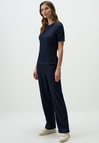 Donkerblauwe textuurtop met korte mouwen, gecombineerd met bijpassende losse broek. De outfit heeft een subtiel geribbeld patroon en zijsplitten.