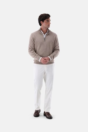 Beige knit sweater with a zip collar, paired with white trousers and dark brown shoes. The outfit features a layered look with contrasting textures.