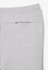 Pantalones de chándal grises con una textura suave, que cuentan con un pequeño bolsillo con cremallera en el lateral y una cinturilla elástica para mayor comodidad.