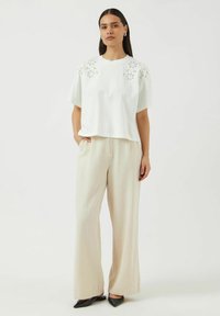 Hvit kortermet topp med blomsterbroderte detaljer, kombinert med lyse beige vide bukser og svarte spisse sko; avslappet passform.