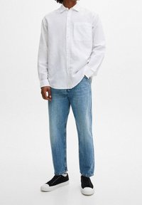 Vit långärmad skjorta med knappar fram och bröstficka, ihop med ljusblå jeans och svarta sneakers med vita sulor.