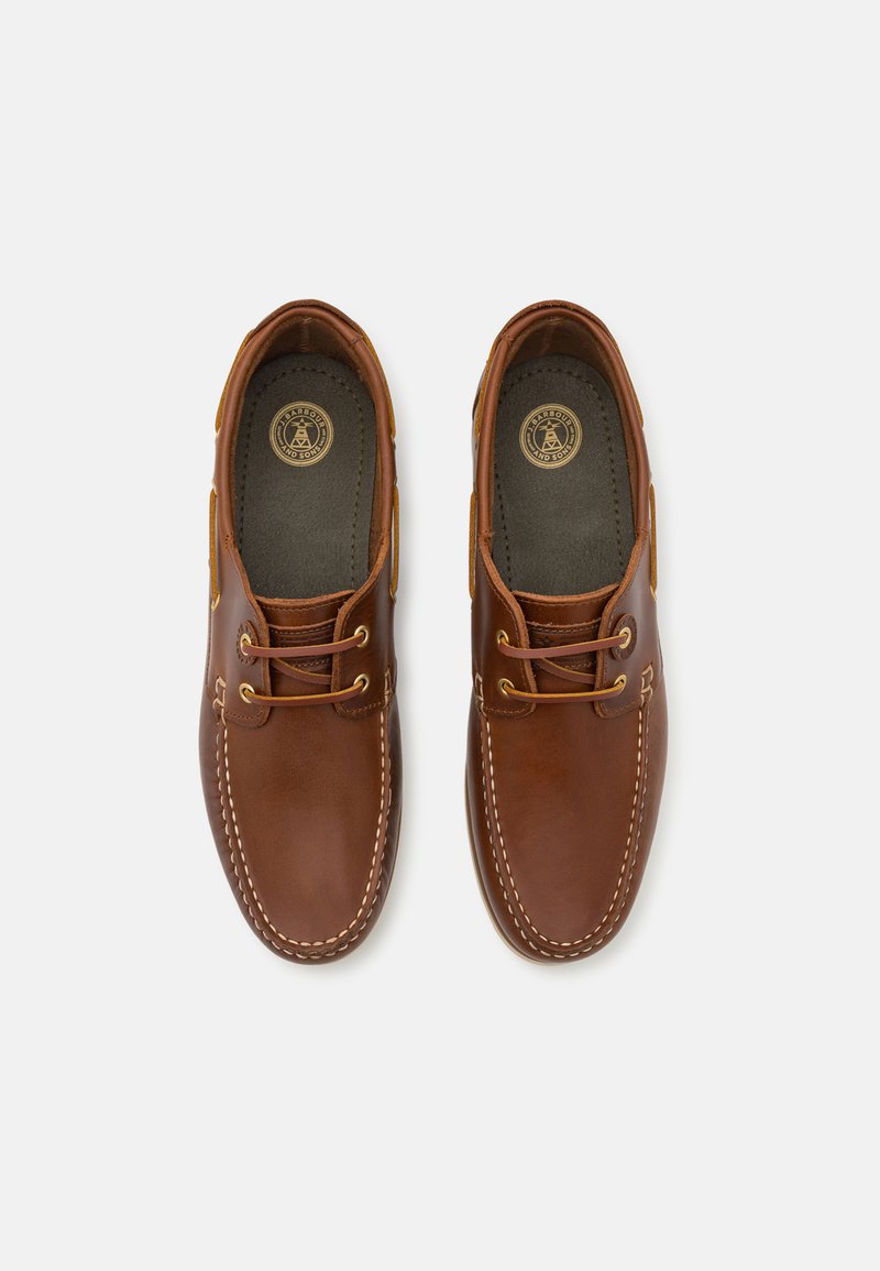 Bateaux en cuir marron avec une finition lisse, bout rond et détails de couture blanche. Œillets dorés pour les lacets. Semelle intérieure rembourrée de couleur foncée.