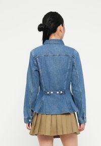 Jeansjakke med et slankt design, lys blå farge, knappeakenter ved midjen, og standard krage. Teksturert stoff med synlig søm.