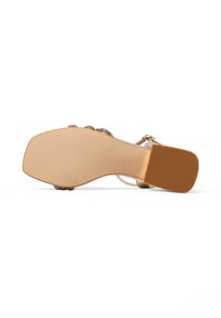 Sandal con tacco beige caratterizzata da una tomaia testurizzata, cinturini decorativi e una suola liscia con un'altezza del tacco moderata.