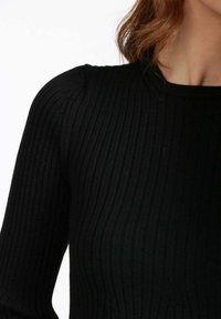 Top in maglia nera a coste con maniche lunghe e collo rotondo, caratterizzato da un tessuto testurizzato che mette in risalto il design attillato.