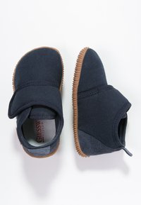 Marineblauwe instapschoenen met een geweven bovenkant van stof, rubberen zool en klittenbandsluiting. Beschikt over een grijze accent op de hak.