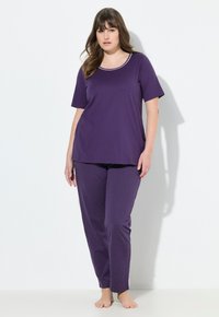 Top da pigiama viola a maniche corte con scollatura bianca, abbinato a pantaloni viola con pois. Realizzato in un tessuto morbido e leggero.