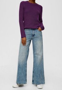 Fialový žebrovaný svetr spojený s džíny světle modrého odstínu se širokými nohavicemi. Oblečení má volný střih a jemné texturované detaily.