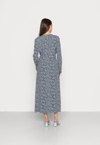 Vestido florido azul marinho de mangas longas, com uma cintura ajustada, saia até os tornozelos e um padrão subtil de flores brancas. Combinado com sapatos de salto bloco azul claro.