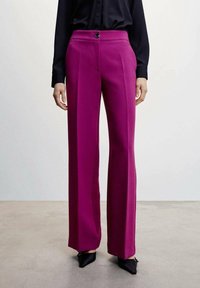 Magenta wijde broek gemaakt van een gladde stof, met een knoop aan de voorkant en plooien, gecombineerd met een zwart overhemd met knopen.