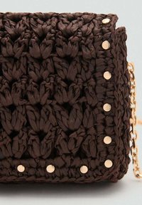 Sac tissé marron fabriqué à partir d'un matériau texturé, avec des rivets dorés sur un côté et une bandoulière en chaîne dorée. Forme compacte et rectangulaire.