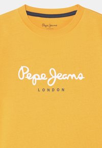 Żółta bawełniana koszulka z okrągłym dekoltem, z białym, cursywnym logo "Pepe Jeans" oraz napisem "LONDYN" wydrukowanym na szaro poniżej.