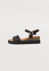 Sandales noires ouvertes avec une bride de cheville, boucle dorée, semelle intérieure rembourrée couleur beige et semelle compensée à motif tissé.