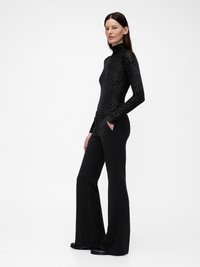 Μαύρο κορμάκι με μακριά μανίκια και υφή λεοπάρ, συνδυασμένο με μαύρο καμπάνα παντελόνι, με τσέπες και λεία επιφάνεια.