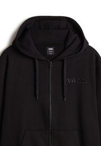 Schwarzer Kapuzenpullover mit Reißverschluss, Kapuze und Kordeln, mit einem tonalen Vans-Logo auf der linken Brust und vorderen Kängurutaschen.