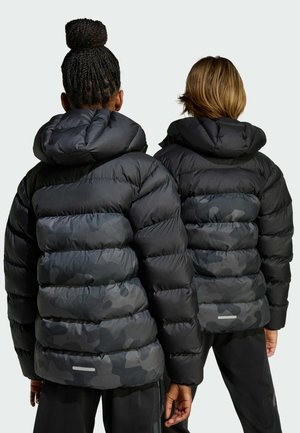 Les vestes matelassées noires avec capuchon présentent des sections en camouflage sombre contrastantes, un design matelassé et des accents réfléchissants le long de l'ourlet.