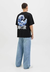 Camiseta negra con un gráfico de ola azul en la parte posterior y texto en japonés. Combinada con unos vaqueros baggy de color azul claro, que muestran un ajuste relajado.