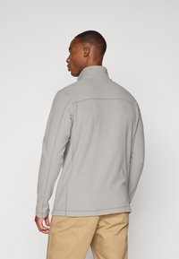 Sudadera de felpa gris con cuello alto y mangas largas, con costuras cosidas y un ajuste relajado, combinada con pantalones beiges.