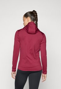 Bordeauxroter langärmeliger Hoodie mit hochgeklapptem Kragen, dehnbarem Stoff, tailliertem Schnitt und glatter Textur. Getragen mit schwarzen Leggings, Rückansicht.