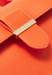 Sac en similicuir orange à la texture lisse, doté d'une plaque logo ANNA FIELD en ton or et d'une fermeture à rabat sécuris ée.