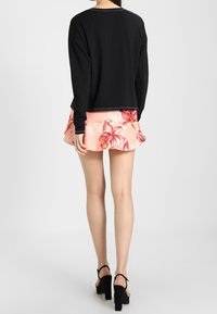 Svart långärmad topp, ljusrosa blommig skaterkjol med volangkant. Svarta högklackade sandaler. Enkelt mönster och avslappnad stil.