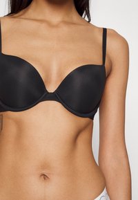 Black padded bra with thin straps, smooth fabric, and a plunge neckline. Features a seamless design and subtle stitching details.