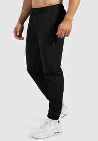 Zwarte joggers met een elastische tailleband, twee zijzakken en een slim fit. Gecombineerd met witte sneakers voor een sportieve uitstraling.