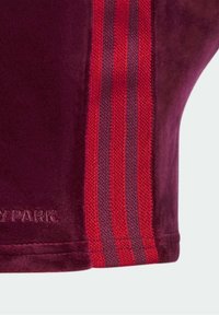 Sammet i bordeaux med röda och grå randiga detaljer. Har sömnadsdetaljer och en logo präglad längst ner. Strukturerad yta.