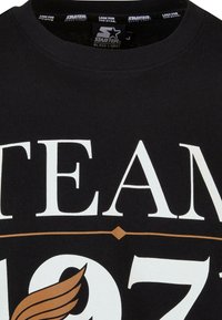 Tricou negru cu text alb mare care spune "ECHIPA" și "1971," cu un grafic decorativ de aripă aurie și guler rotund.