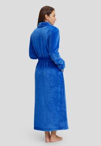 Bata de felpa azul con cuello chal, mangas largas, cinturón en la cintura y bolsillos. Textura suave con un color sólido y diseño hasta el suelo.