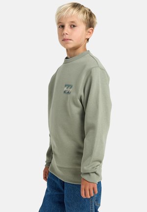 Green sweatshirt with round neck, ribbed cuffs, and hem. Features a small wave graphic in blue and cream on the front. Denim jeans.