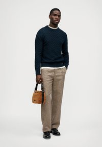 Marineblauer Strickpullover mit struktuierter Musterung, beigefarbene Wollhose und eine braune flauschige Handtasche. Schwarzen glänzende Schuhe runden den Look ab.