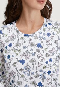 Camicia bianca a maniche lunghe con stampa floreale a tutto campo in blu, verde e viola, col collo rotondo e una texture morbida.