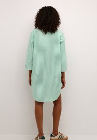 Sukienka w zielono-białe paski z rękawami o długości trzy czwarte, zaokrąglonym dołem i luźnym krojem, wykonana z lekkiego materiału.