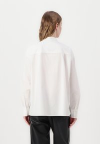 Chemise blanche à manches longues avec un col classique et une coupe décontractée. Tissu en coton frais, avec des poignets boutonnés et un ourlet droit.