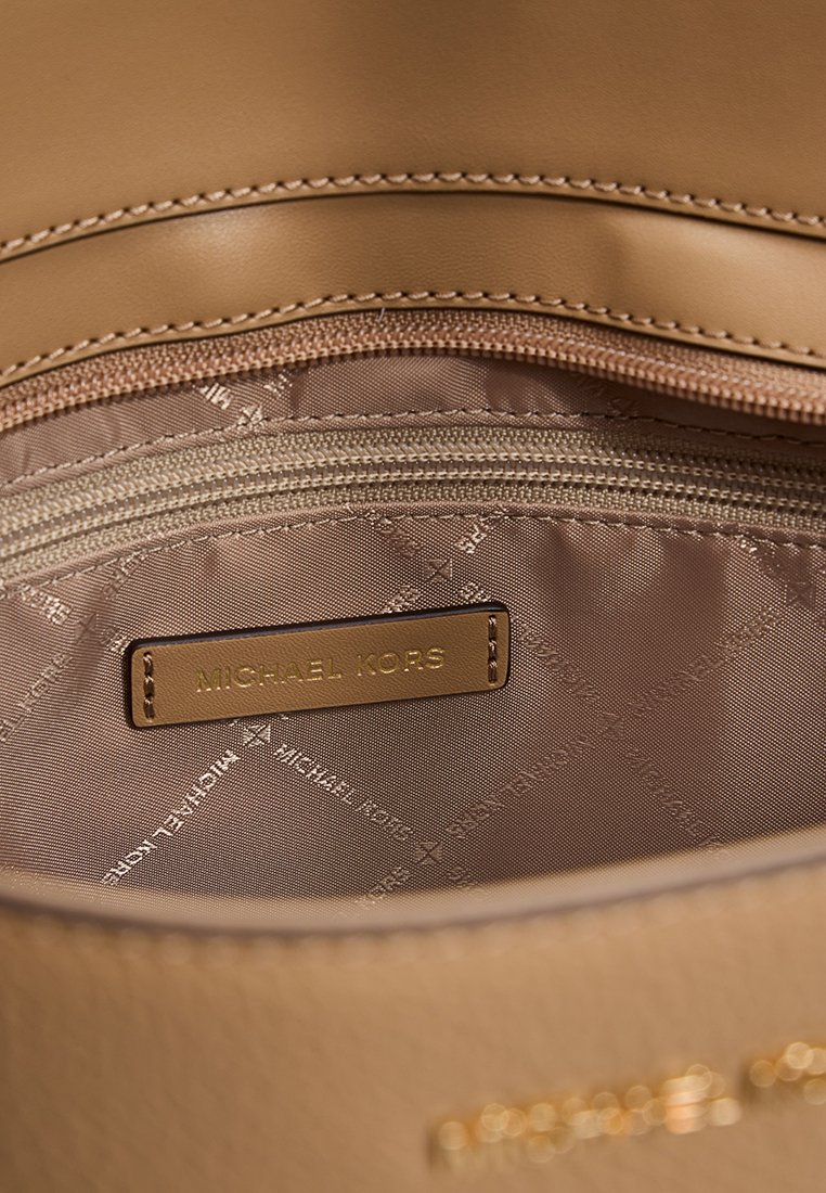 Interno di una borsa in pelle color cuoio con una tasca con zip, dotata di un'etichetta con logo e fodera in tessuto neutro e liscio.