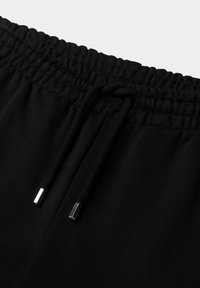 Black sweatpants feature an elastic waistband with a drawstring, metallic tips, and a soft, smooth texture.