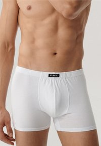 Białe bawełniane bokserki z elastycznym pasem w czarną metkę. Mają dopasowany krój i gładką fakturę.