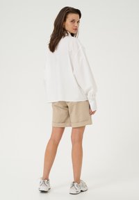 White oversized shirt, beige striped shorts, and gray sneakers. The shirt features long sleeves, and the shorts have a cuffed hem.