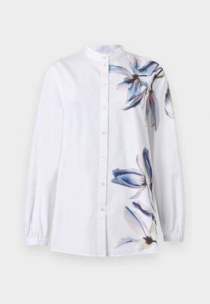 Chemise blanche à manches longues avec boutons et col mandarin, ornée de motifs floraux bleus et violets sur l'épaule droite et le bas du côté gauche.