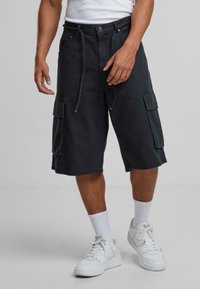 Cargo shorts in dark denim with a relaxed fit, featuring side pockets, drawstring, and contrast stitching. Paired with white sneakers.
