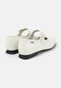 Weiße Leder-Mary-Jane-Schuhe mit einer schwarzen Gummisohle, die ein auffälliges Cut-Out-Design und einen verstellbaren Riemen aufweisen.