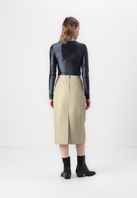 Mørk topp med lange ermer, beige høy midje skjørt med glidelås bak, ankellange svarte høye støvletter med teksturdetaljer.