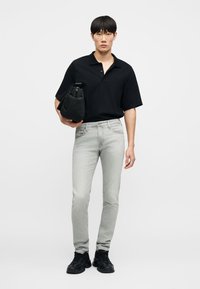 Μαύρο πόλο μπλουζάκι με κοντά μανίκια, ανοιχτό γκρι τζιν στενής γραμμής και μαύρα αθλητικά παπούτσια, κρατώντας μια μαύρη τσάντα. Απλός σχεδιασμός, ουδέτερα χρώματα, καθημερινή εμφάνιση.